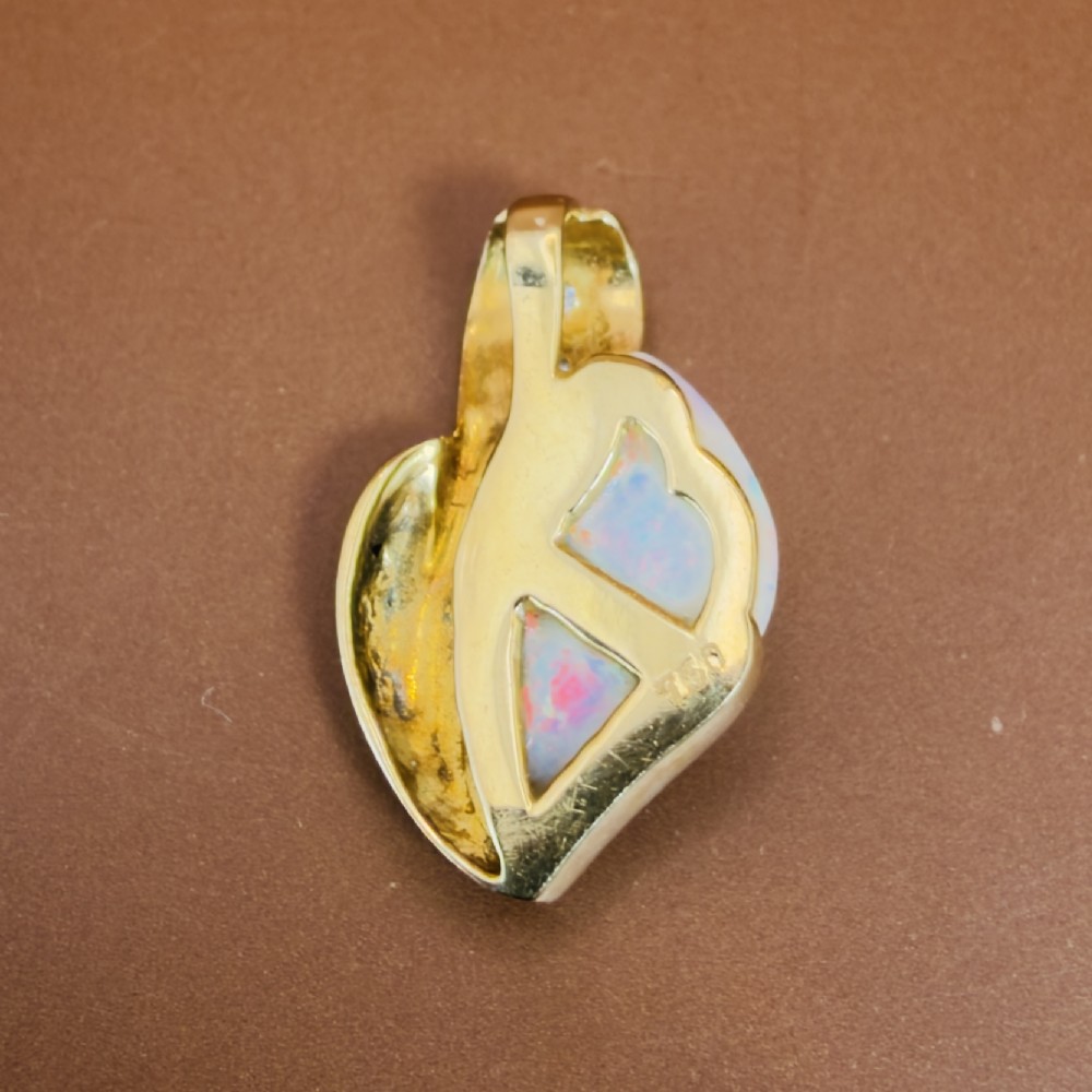 An 18ct yellow gold freeform pendant displaying an iridescent white opal with green and pink flash, set alongside two accent diamonds on the bail. View VII