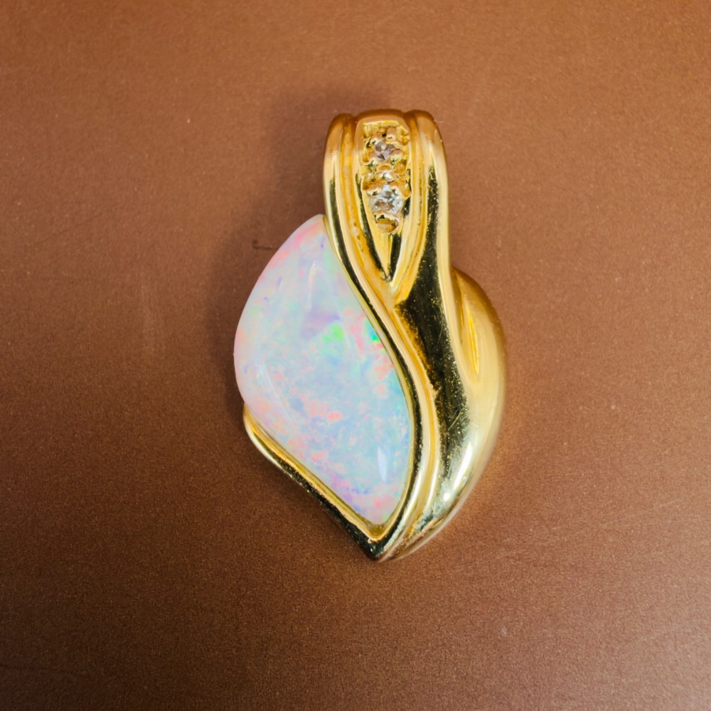 An 18ct yellow gold freeform pendant displaying an iridescent white opal with green and pink flash, set alongside two accent diamonds on the bail. View IX