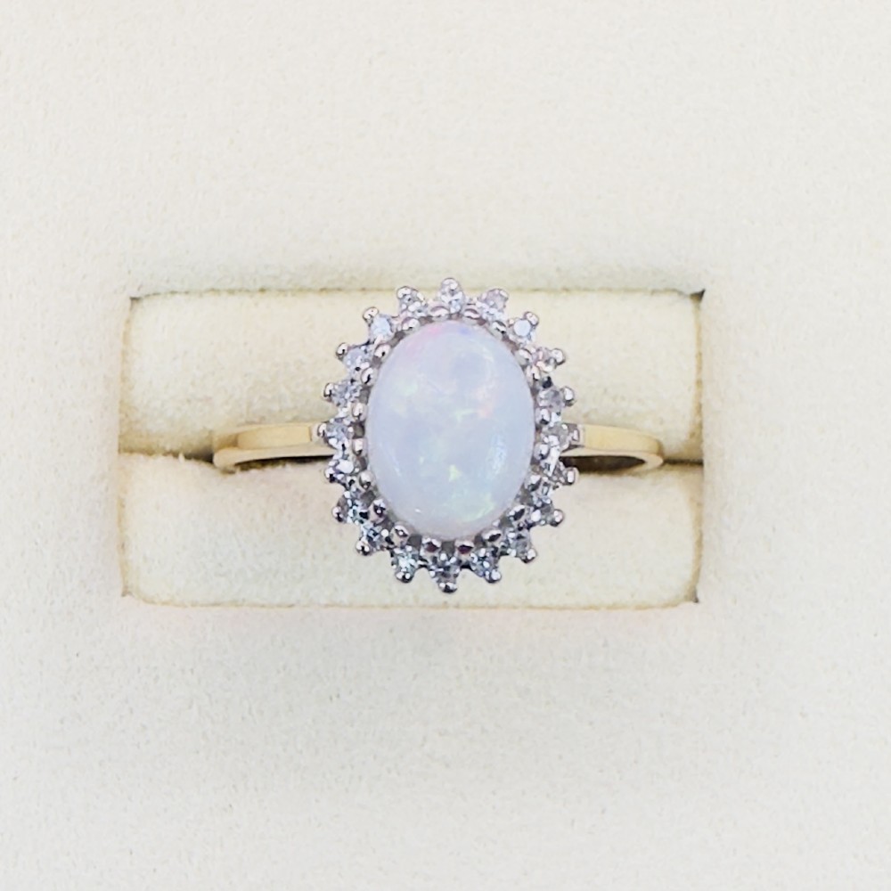 A 9ct yellow gold ring featuring a central oval cabochon opal surrounded by a halo of small claw-set diamonds.