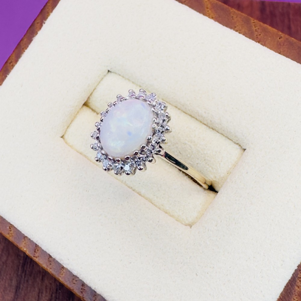 A 9ct yellow gold ring featuring a central oval cabochon opal surrounded by a halo of small claw-set diamonds. View II
