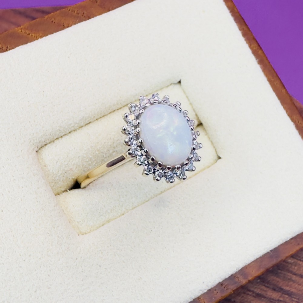 A 9ct yellow gold ring featuring a central oval cabochon opal surrounded by a halo of small claw-set diamonds. View III