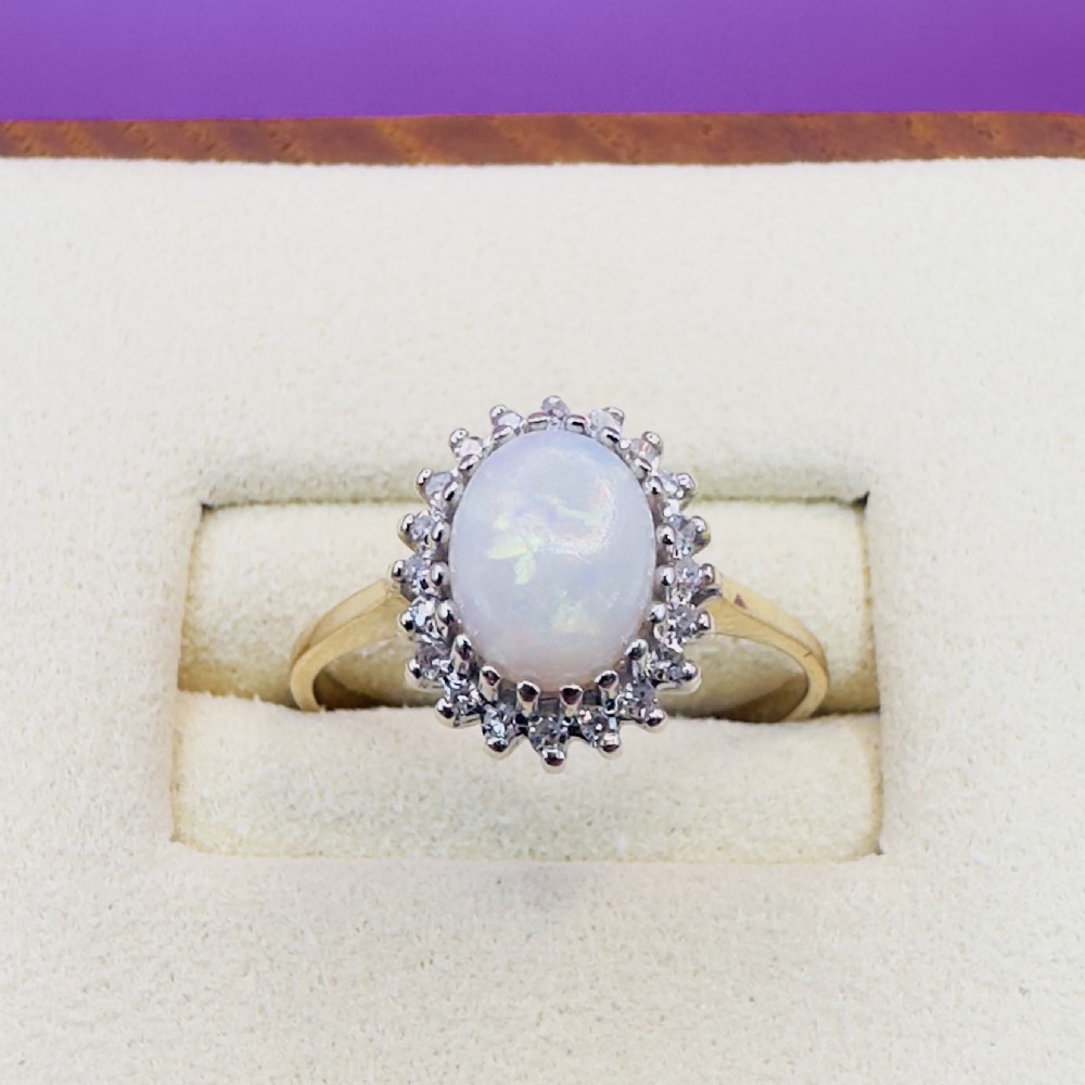 A 9ct yellow gold ring featuring a central oval cabochon opal surrounded by a halo of small claw-set diamonds. View IV
