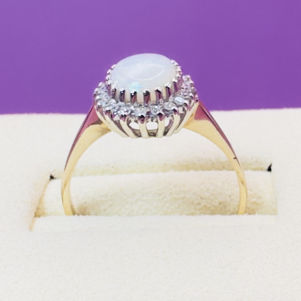A 9ct yellow gold ring featuring a central oval cabochon opal surrounded by a halo of small claw-set diamonds. View V