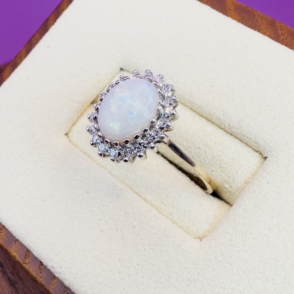 A 9ct yellow gold ring featuring a central oval cabochon opal surrounded by a halo of small claw-set diamonds. View VI