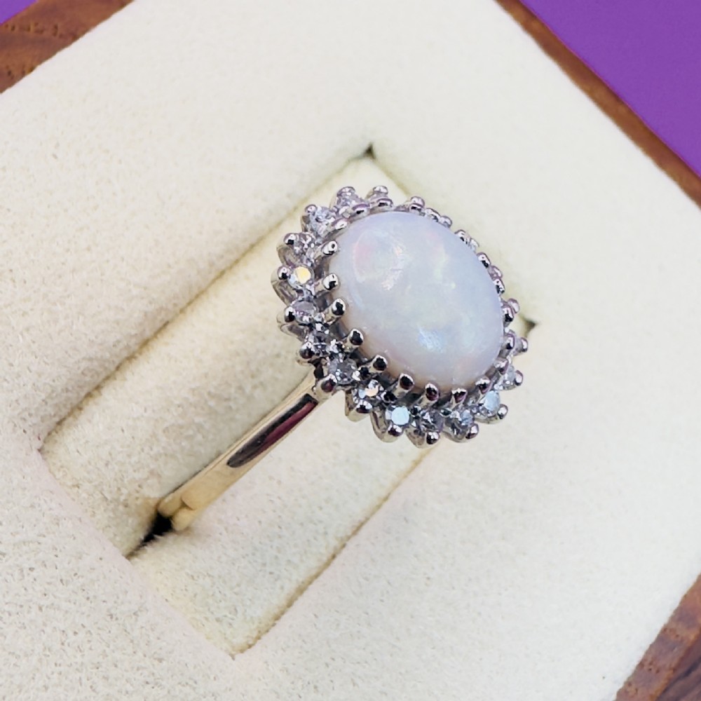 A 9ct yellow gold ring featuring a central oval cabochon opal surrounded by a halo of small claw-set diamonds. View VII