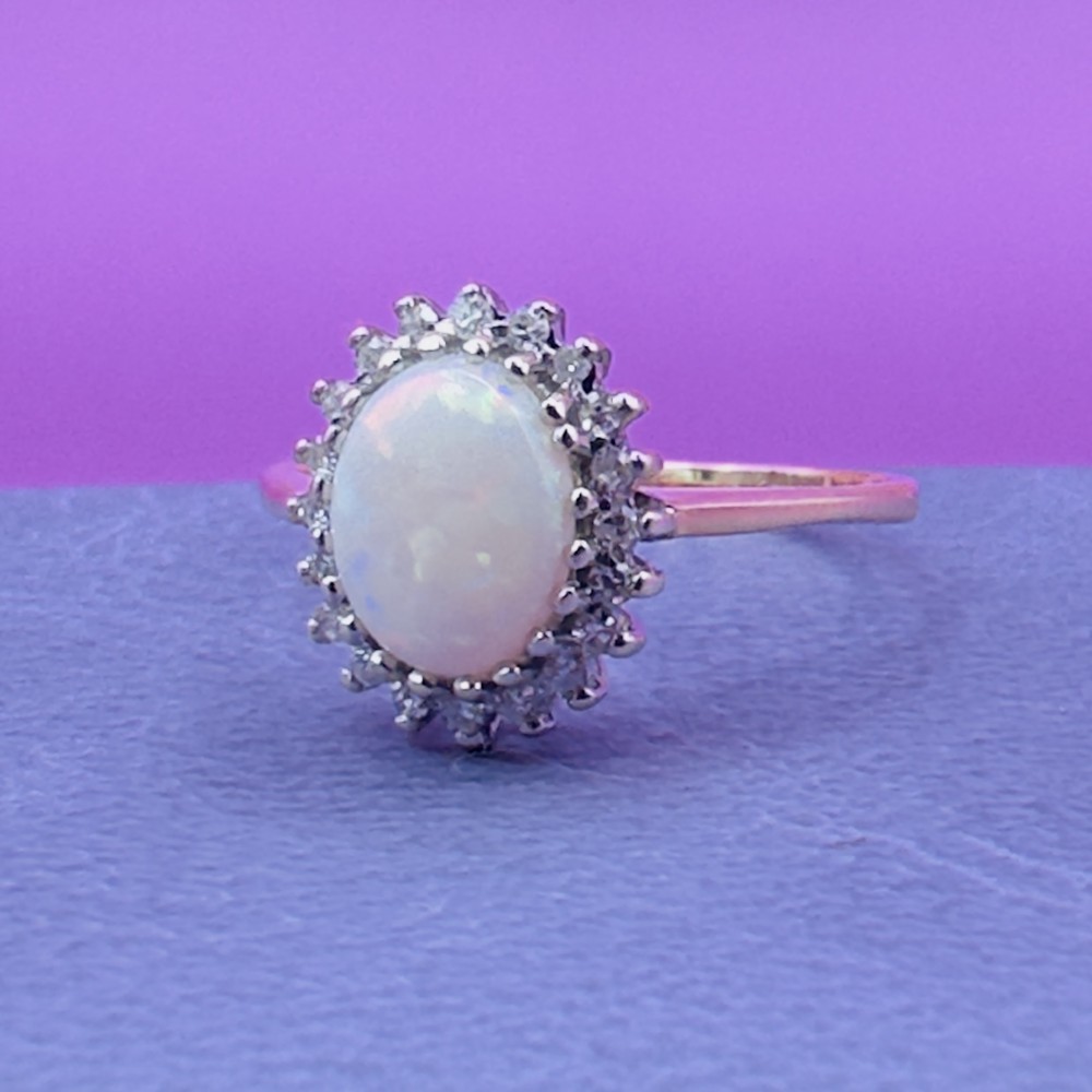 A 9ct yellow gold ring featuring a central oval cabochon opal surrounded by a halo of small claw-set diamonds. View VIII