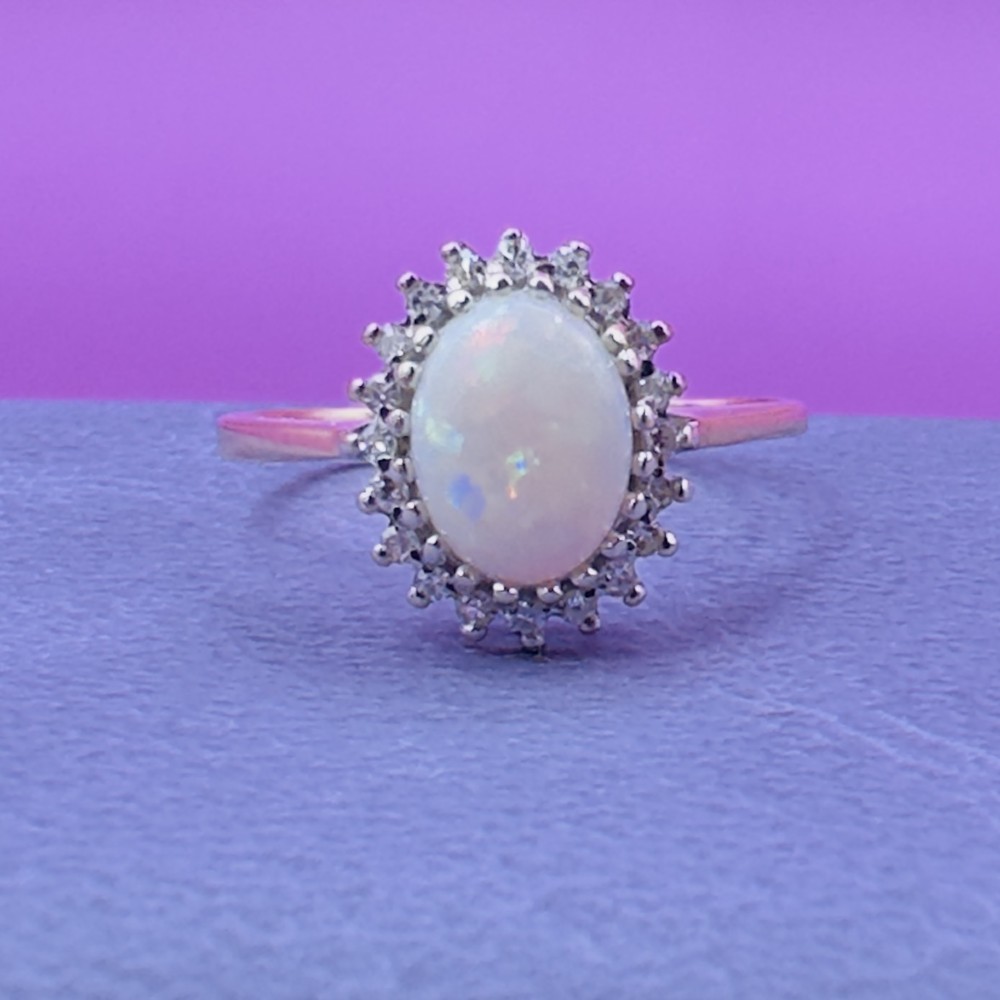 A 9ct yellow gold ring featuring a central oval cabochon opal surrounded by a halo of small claw-set diamonds. View IX