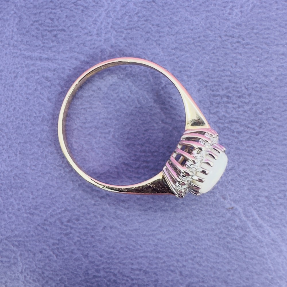 A 9ct yellow gold ring featuring a central oval cabochon opal surrounded by a halo of small claw-set diamonds. View XI
