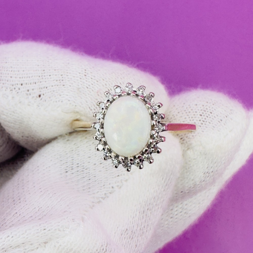 A 9ct yellow gold ring featuring a central oval cabochon opal surrounded by a halo of small claw-set diamonds. View XIII