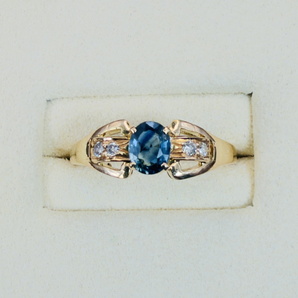 An 18ct yellow gold ring featuring a central oval-cut blue sapphire flanked by round diamonds set into carved shoulders. View II