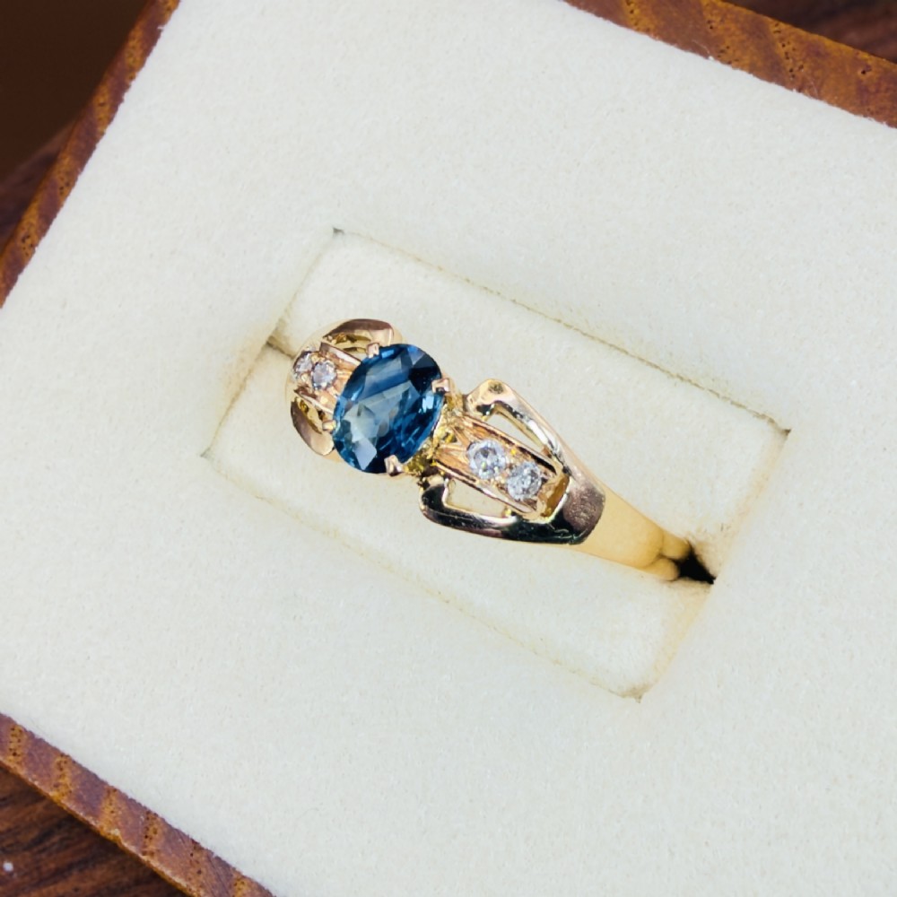 An 18ct yellow gold ring featuring a central oval-cut blue sapphire flanked by round diamonds set into carved shoulders. View III