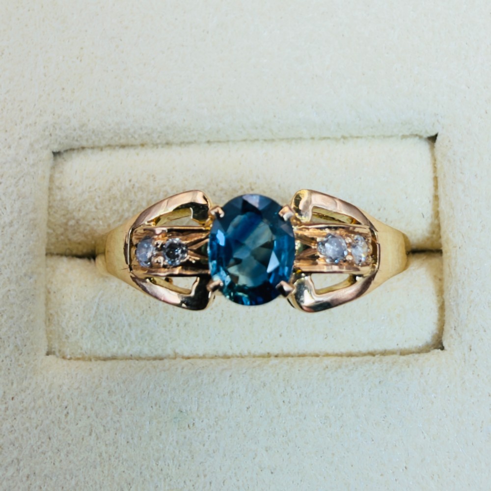 An 18ct yellow gold ring featuring a central oval-cut blue sapphire flanked by round diamonds set into carved shoulders. View V