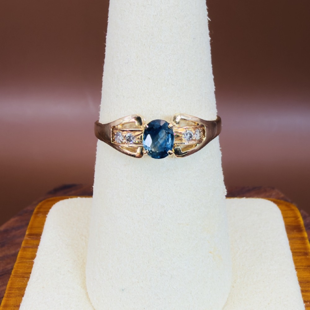 An 18ct yellow gold ring featuring a central oval-cut blue sapphire flanked by round diamonds set into carved shoulders. View VI