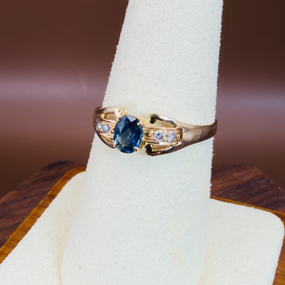 An 18ct yellow gold ring featuring a central oval-cut blue sapphire flanked by round diamonds set into carved shoulders. View VII