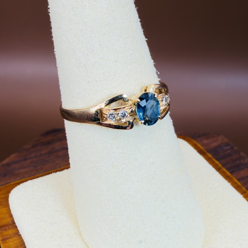 An 18ct yellow gold ring featuring a central oval-cut blue sapphire flanked by round diamonds set into carved shoulders. View VIII