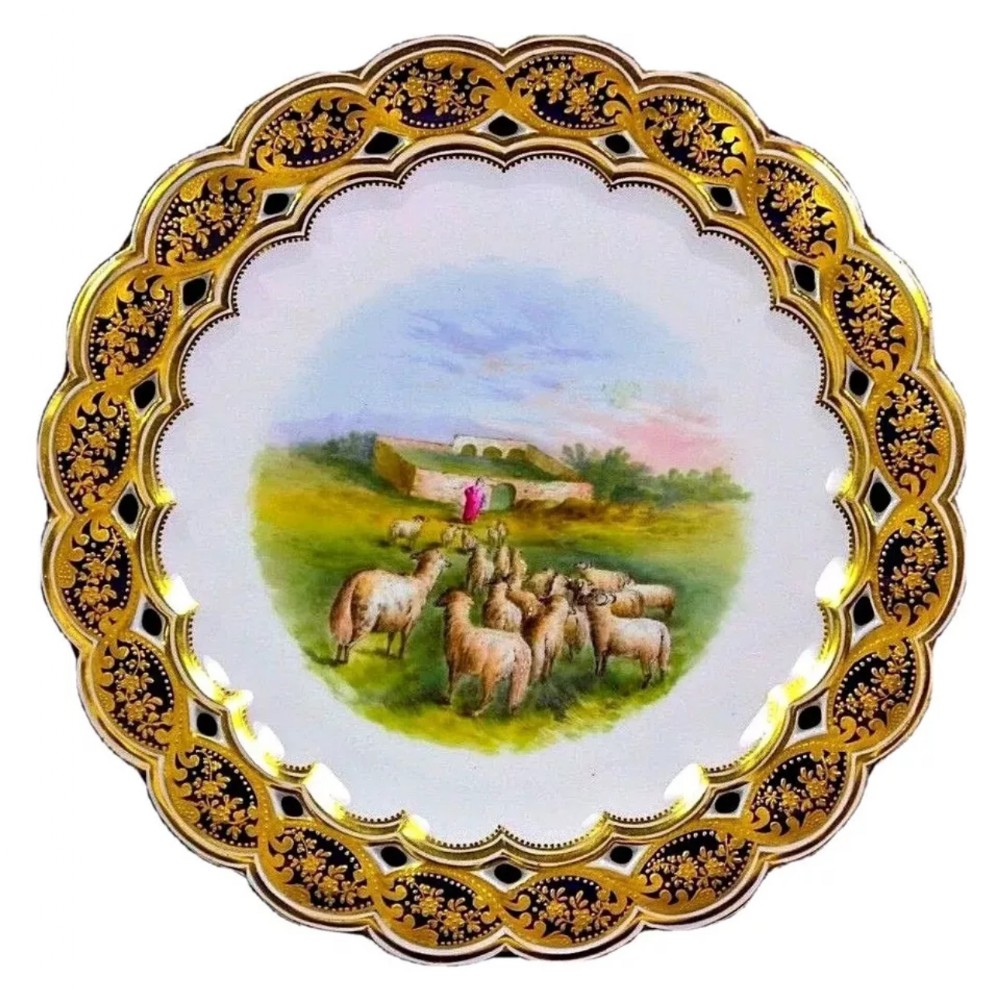 A circular Victorian Coalport porcelain cabinet plate featuring a central hand-painted landscape with sheep and a shepherd, bordered by an intricate reticulated gilt and cobalt blue rim.