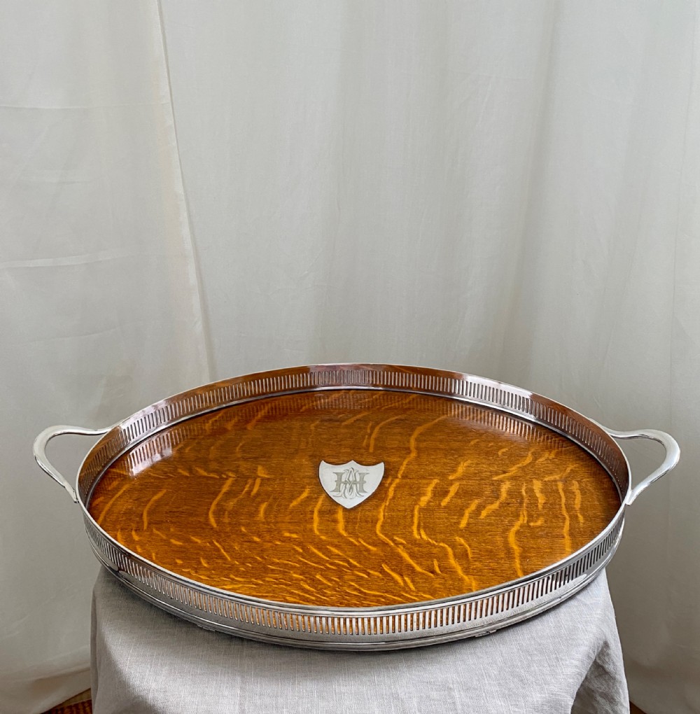 An oval 19th-century quarter-sawn oak gallery tray featuring a pierced silver-plated rim, central engraved shield plaque, and side carrying handles.