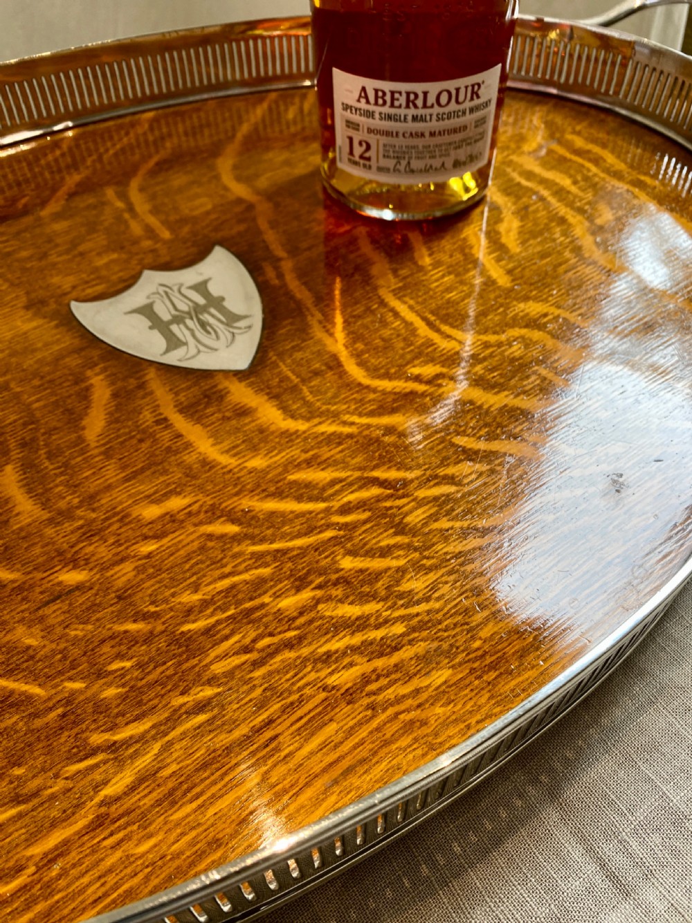 An oval 19th-century quarter-sawn oak gallery tray featuring a pierced silver-plated rim, central engraved shield plaque, and side carrying handles. View VII