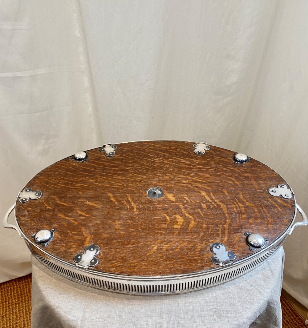 An oval 19th-century quarter-sawn oak gallery tray featuring a pierced silver-plated rim, central engraved shield plaque, and side carrying handles. View X