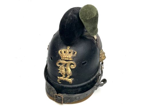 fig 1. An antique black leather Imperial German military helmet featuring a crowned monogram brass plate, lion head side bosses, and a dense black and green woolen crest.