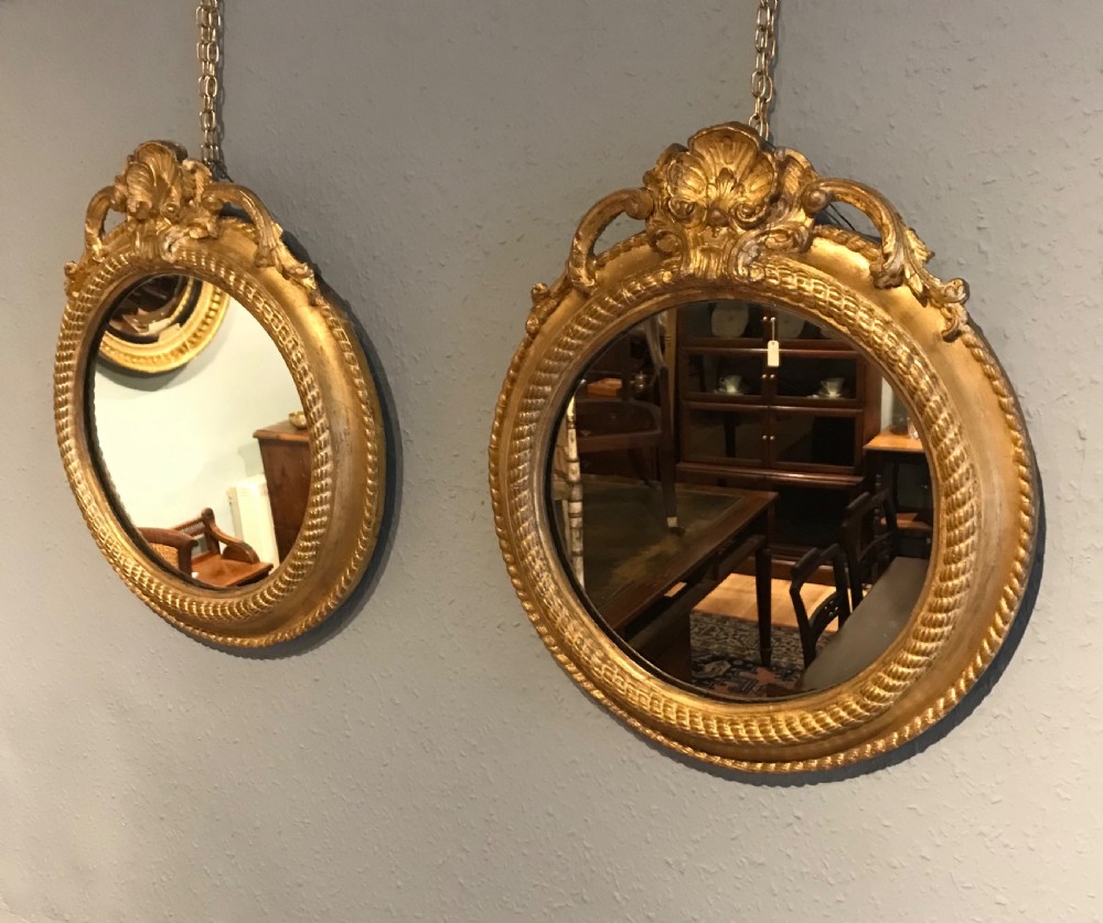 A pair of circular wall mirrors featuring carved gilt frames with top shell pediments, rope-twist inner borders, and chain suspensions. View II
