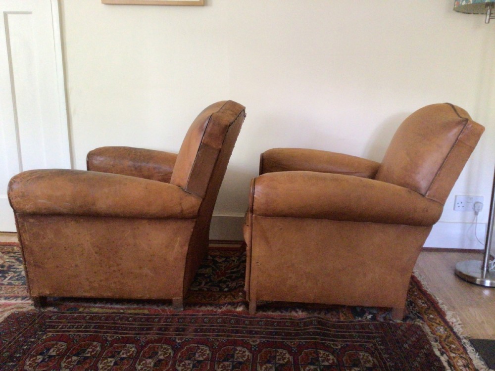 A pair of Art Deco tan leather club armchairs featuring rolled armrests, arched backrests, and aged surface patina. View VIII