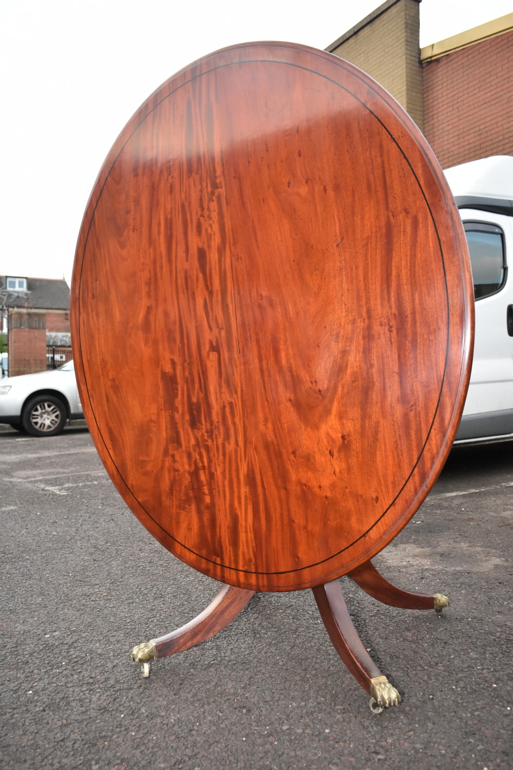 A Regency mahogany tilt-top oval breakfast table featuring ebony line inlay around the perimeter and a central pedestal with splayed quadruped legs terminating in brass claw castors. View III