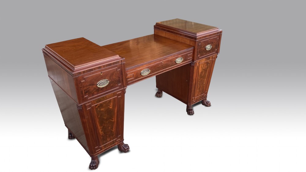 An antique Regency flame mahogany twin pedestal sideboard featuring stepped pedestal cupboards, central drawers, brass drop handles, and carved paw feet.