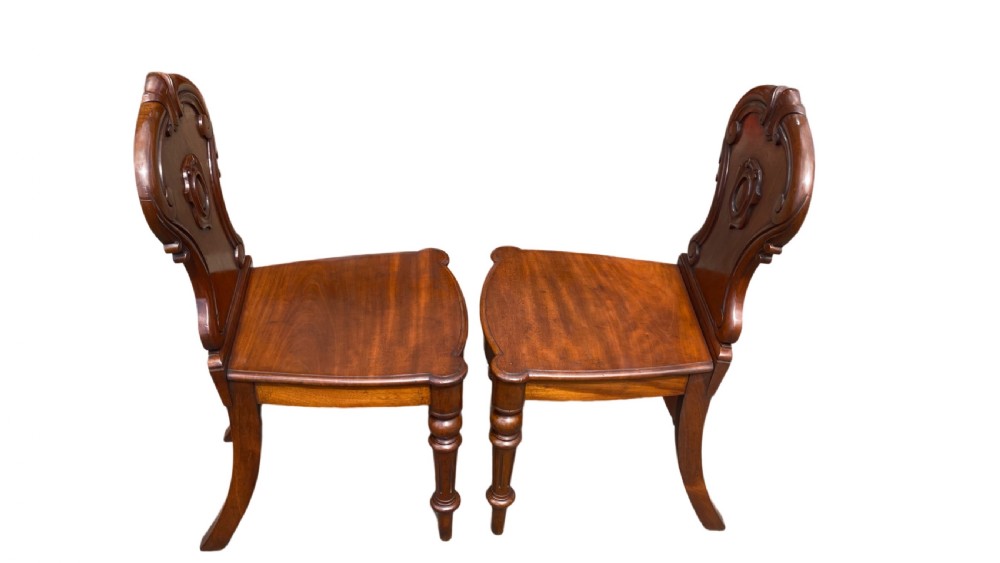 A pair of 19th-century William IV mahogany hall chairs featuring carved cartouche backrests, solid timber seats, and turned front legs. View II