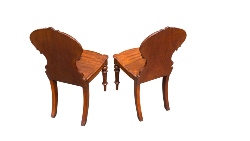 A pair of 19th-century William IV mahogany hall chairs featuring carved cartouche backrests, solid timber seats, and turned front legs. View III