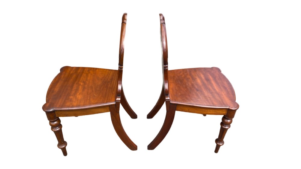 A pair of 19th-century William IV mahogany hall chairs featuring carved cartouche backrests, solid timber seats, and turned front legs. View V