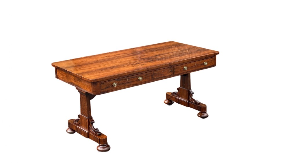 A late Regency rosewood library table featuring frieze drawers with brass handles on trestle end supports. View II
