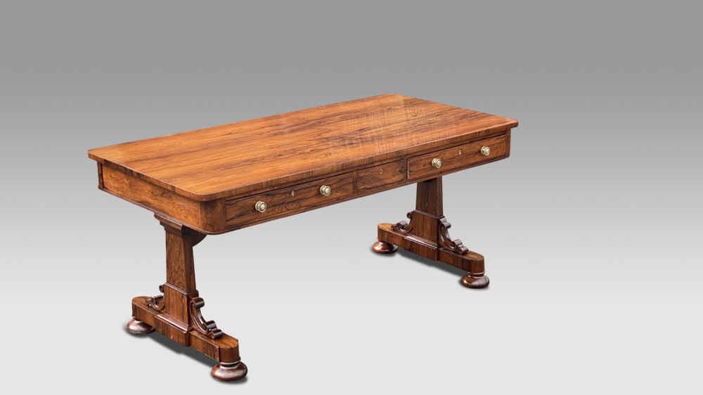 A late Regency rosewood library table featuring frieze drawers with brass handles on trestle end supports.