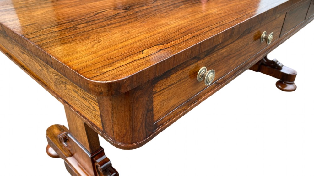 A late Regency rosewood library table featuring frieze drawers with brass handles on trestle end supports. View VII