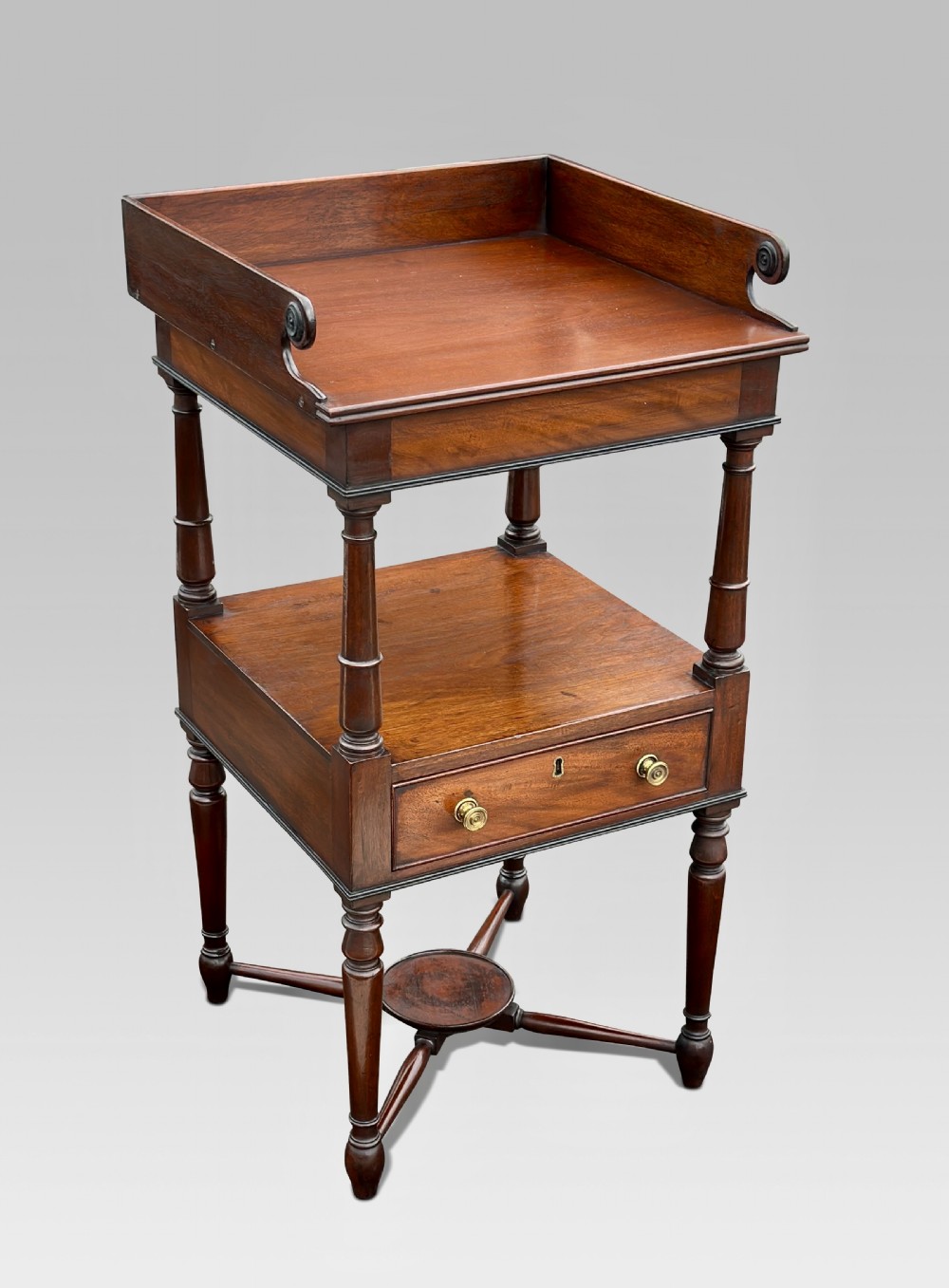 A Regency mahogany two-tier nightstand featuring a galleried top, turned legs with ebonised detailing, a single drawer with brass knobs, and an X-frame stretcher.