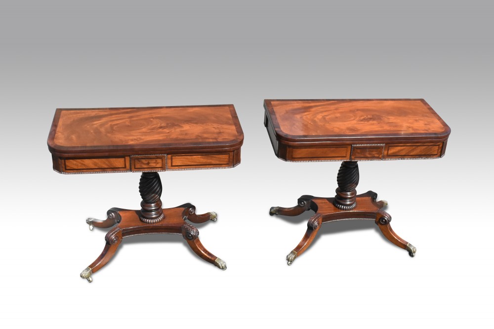 A pair of Regency mahogany fold-over card tables featuring rosewood crossbanding, spiral turned pedestals, and quadripartite legs with brass paw castors. View VI