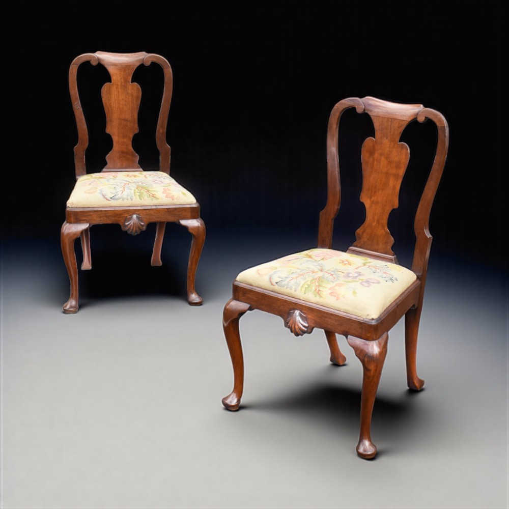 A pair of antique Irish George II red walnut side chairs with vase-shaped back splats, shell-carved aprons, cabriole legs, and floral needlepoint seats.