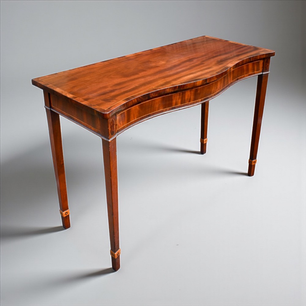 A George III mahogany serpentine console table featuring decorative inlay along the apron and four square tapered legs.