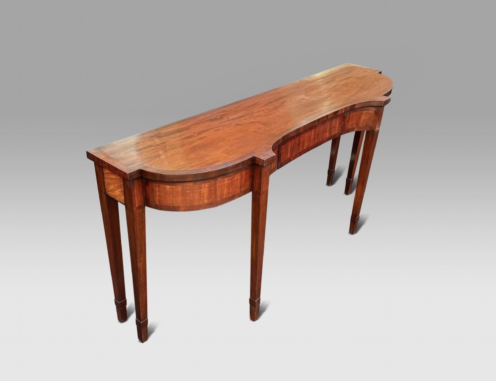 A Georgian mahogany serving table featuring a curved front apron, flame mahogany veneers, and four square tapered legs.
