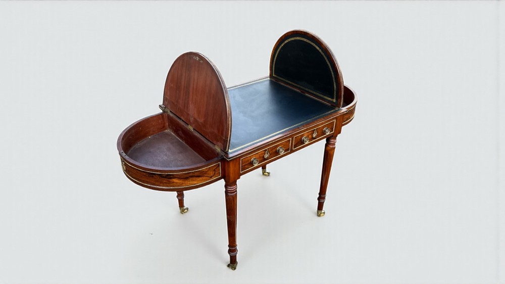 A Regency rosewood writing table featuring a dark leather inset top with brass beaded borders, frieze drawers, rounded ends, and turned legs on brass castors. View XI