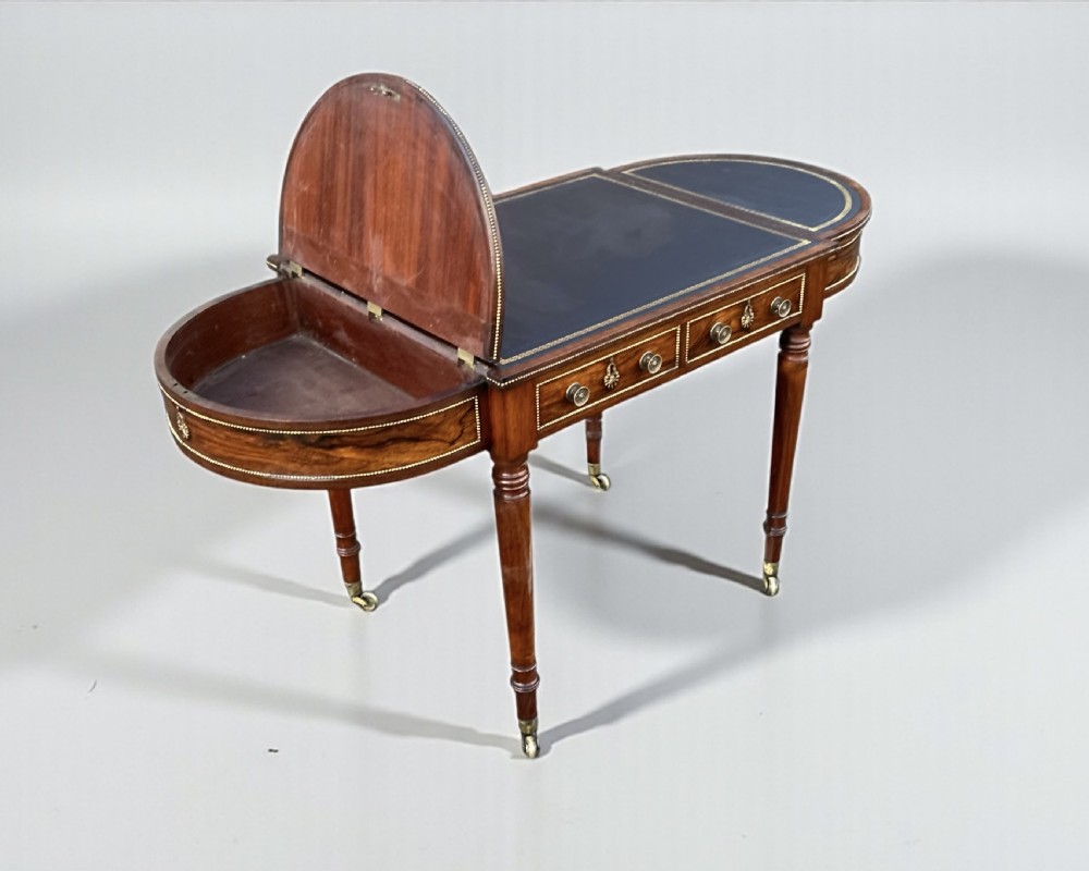 A Regency rosewood writing table featuring a dark leather inset top with brass beaded borders, frieze drawers, rounded ends, and turned legs on brass castors. View XIII