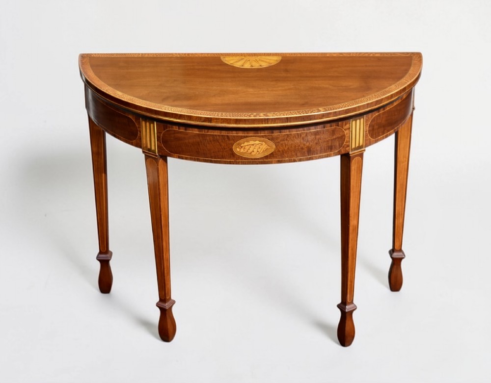 A George III mahogany demi-lune card table featuring fan marquetry, floral oval inlay, decorative stringing, and square tapered legs.