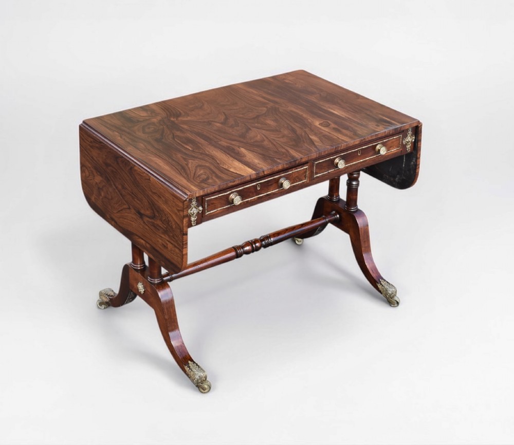 A Regency rosewood sofa table featuring drop-leaf sides, brass inlay, two frieze drawers, and splayed legs on brass castors.