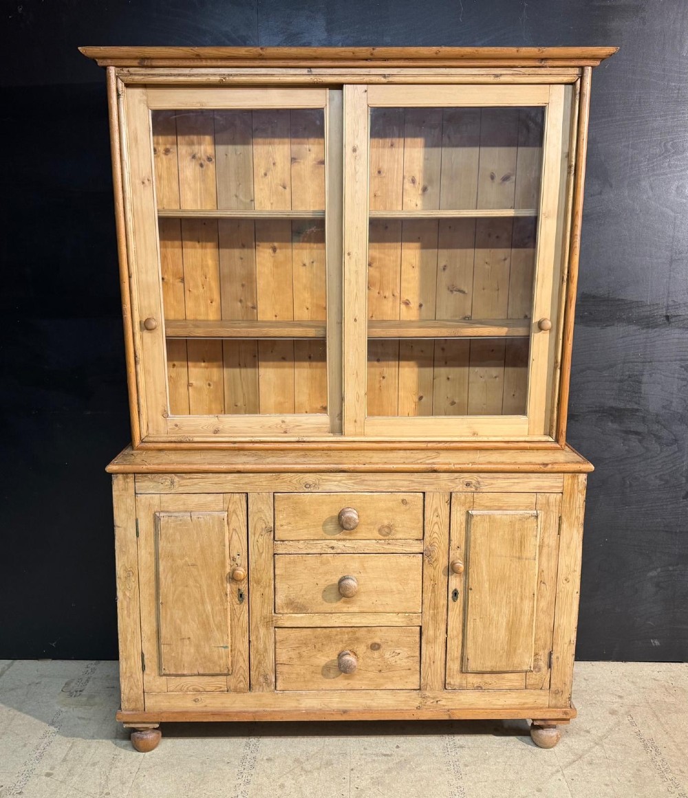 A two-tier warm pine kitchen dresser featuring an upper glazed two-door cabinet with shelves over a lower base containing three central drawers and two side cupboards.