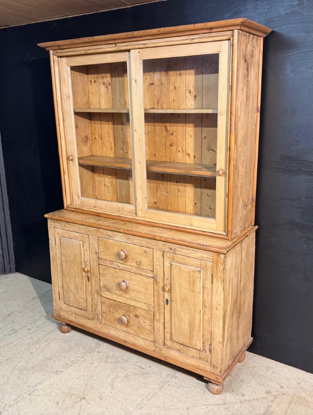 A two-tier warm pine kitchen dresser featuring an upper glazed two-door cabinet with shelves over a lower base containing three central drawers and two side cupboards. View II