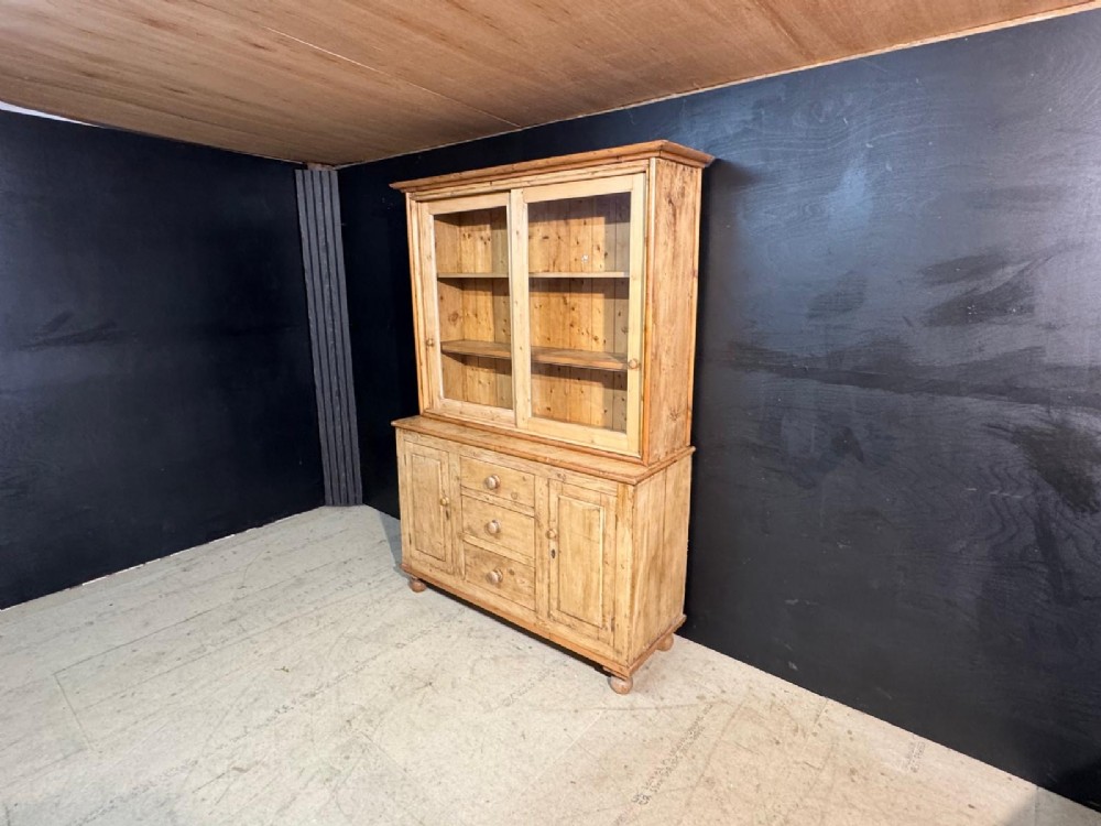 A two-tier warm pine kitchen dresser featuring an upper glazed two-door cabinet with shelves over a lower base containing three central drawers and two side cupboards. View III
