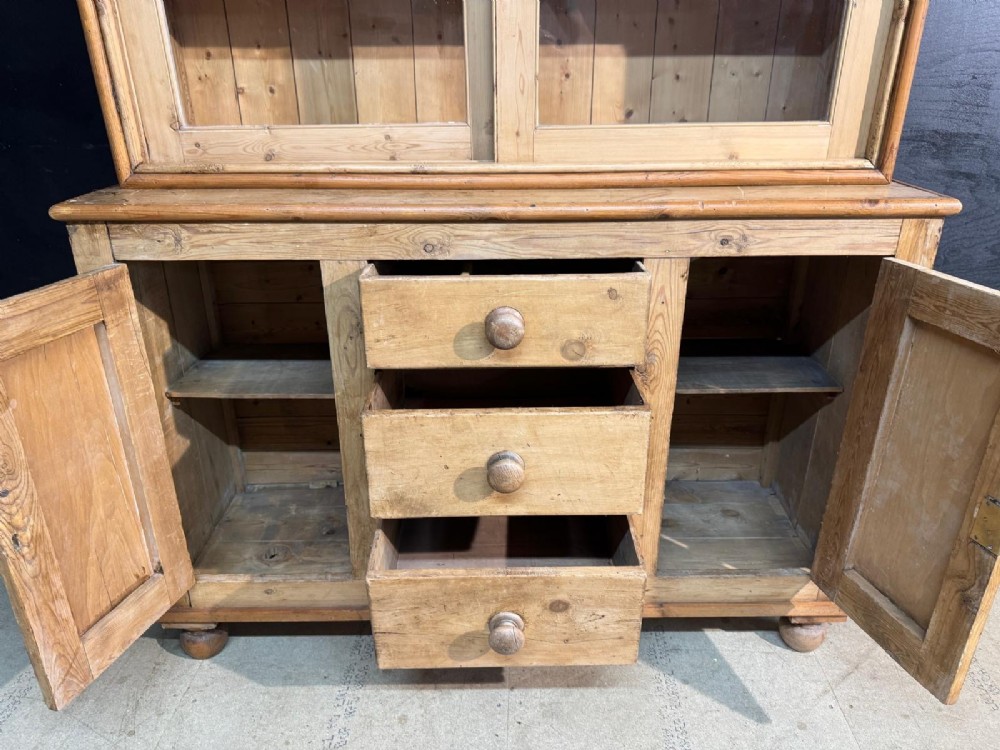 A two-tier warm pine kitchen dresser featuring an upper glazed two-door cabinet with shelves over a lower base containing three central drawers and two side cupboards. View VI