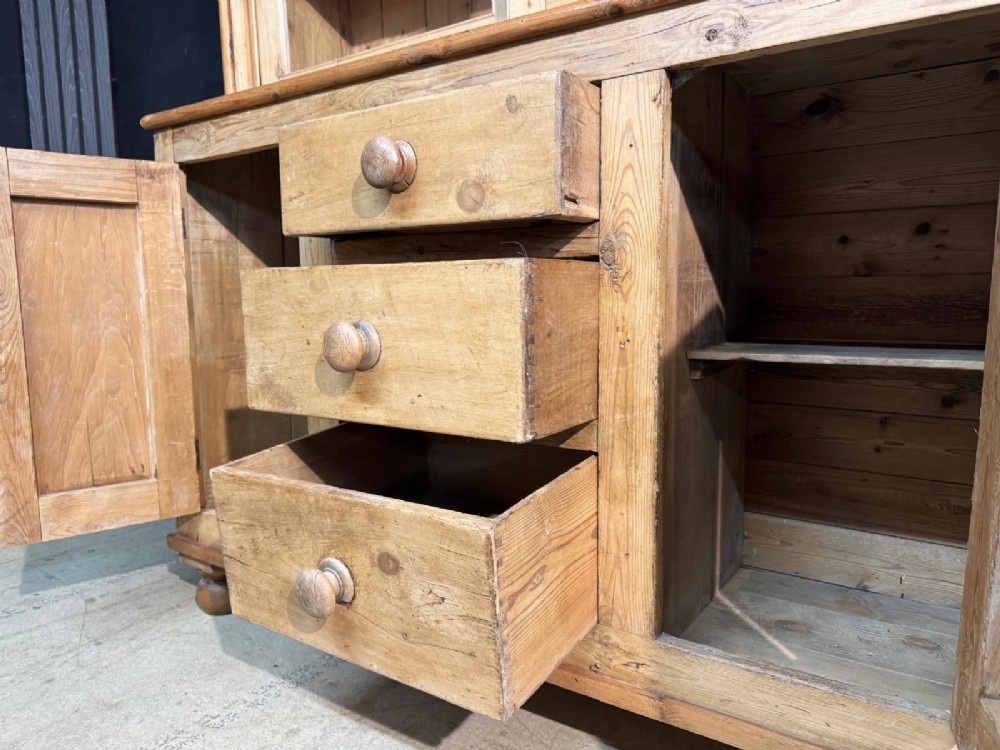 A two-tier warm pine kitchen dresser featuring an upper glazed two-door cabinet with shelves over a lower base containing three central drawers and two side cupboards. View VII