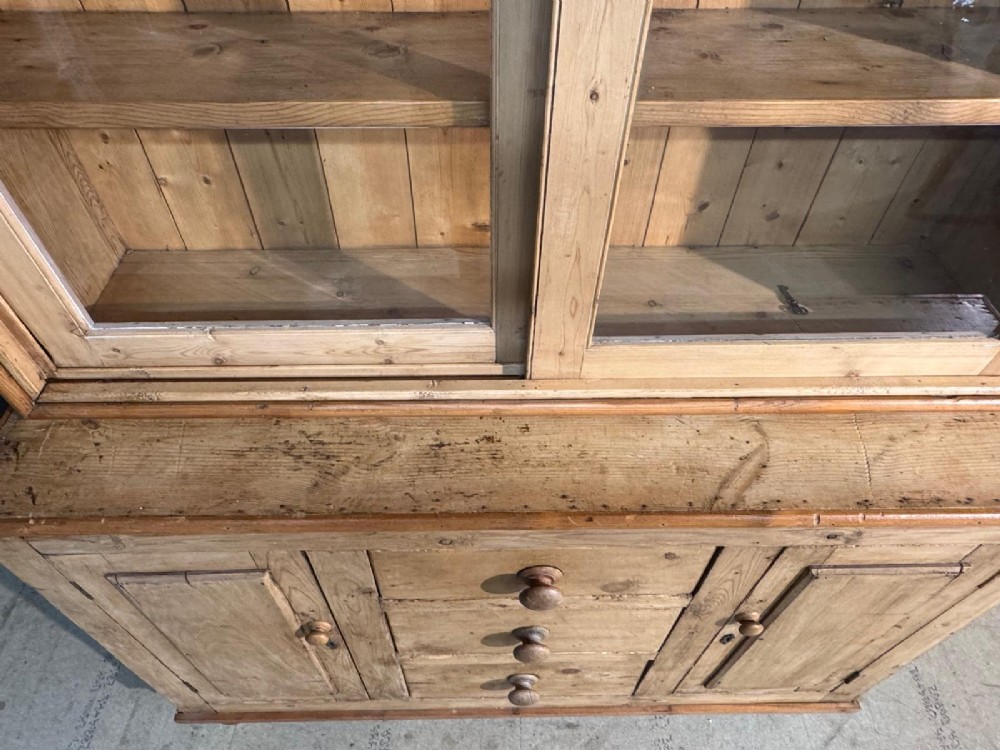 A two-tier warm pine kitchen dresser featuring an upper glazed two-door cabinet with shelves over a lower base containing three central drawers and two side cupboards. View X