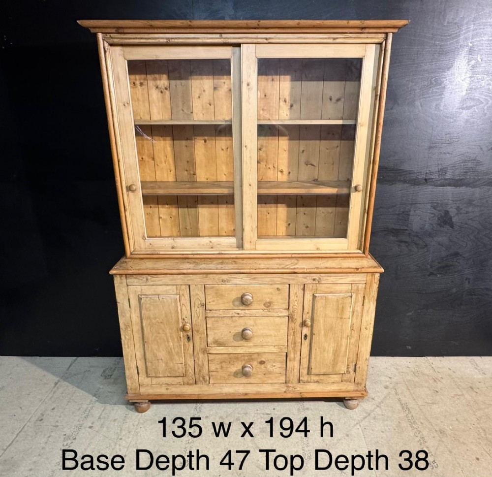 A two-tier warm pine kitchen dresser featuring an upper glazed two-door cabinet with shelves over a lower base containing three central drawers and two side cupboards. View XI